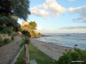 Strand mit Küstenturm hinter grünen Büschen