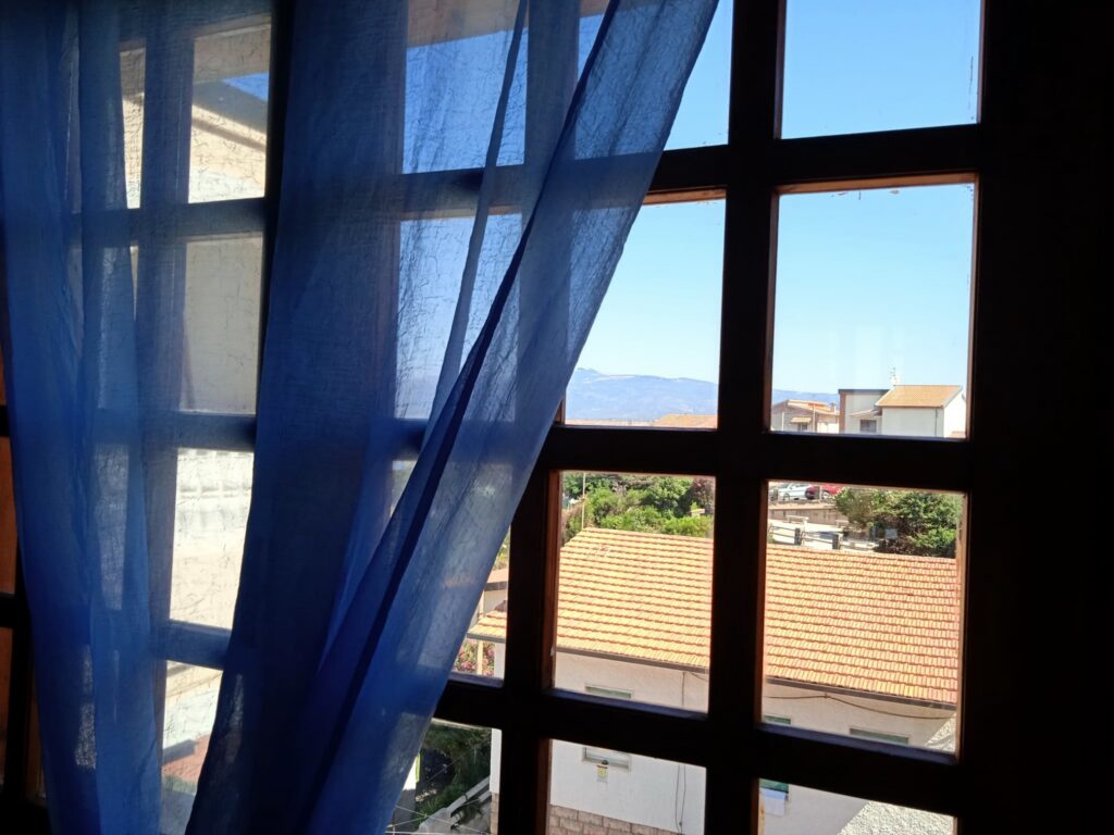 Agrustos Mare, Budoni: Fenster mit blauen Vorhängen und Meerblick Agrustos Mare, Budoni: Fenster mit blauen Vorhängen und Meerblick